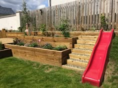 a red slide is in the middle of a wooden planter box with plants growing on it