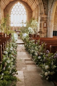 an aisle lined with flowers and pews next to a large window in a church