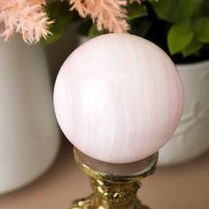 a pink glass ball sitting on top of a golden stand next to a potted plant