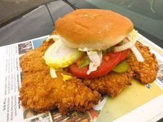 fried chicken sandwich with lettuce tomato and onion on newspaper next to car window