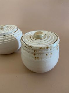 two white bowls with lids are sitting on a brown surface, one is empty and the other has rust