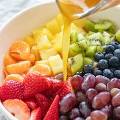 someone pouring orange juice into a bowl full of fruit for a healthy salad or dessert