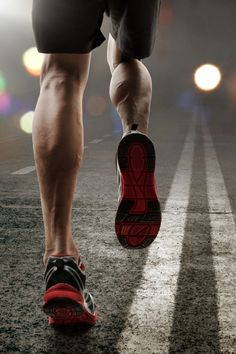 a close up of a person's feet and running shoes on a road with bright lights in the background