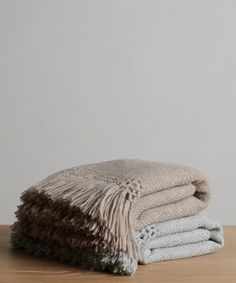 two blankets stacked on top of each other in front of a white wall and wooden table