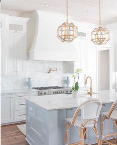 a kitchen with white cabinets and light blue island countertops, gold pendants hanging from the ceiling