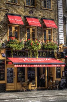 the outside of a restaurant with red awnings and flowers on it's windows