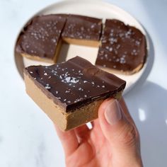 a person holding up a piece of chocolate to show it's side on a plate