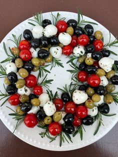 a white plate topped with olives, tomatoes and mozzarella cheese wreath on top of a wooden table