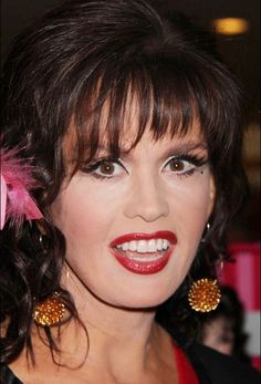 a woman with dark hair and red lipstick wearing large gold earring earrings on her head