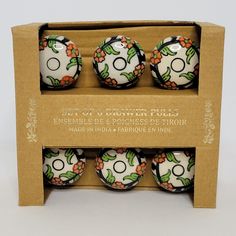 four white and black decorated balls in a cardboard box with orange flowers on the top