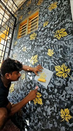 a man is painting a wall with yellow flowers on black and white paper in front of a window