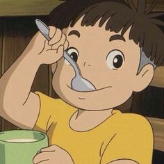 a young boy holding a spoon in his mouth while eating from a green cup on the table