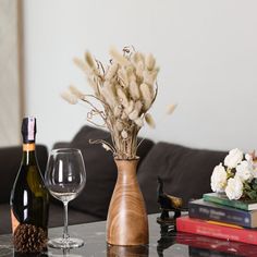 a table topped with two wine glasses and a vase filled with dried flowers next to a bottle of wine