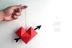 a hand holding a red origami heart with an arrow on it and the words i love you above it