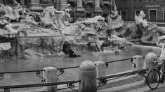 an old black and white photo of a man on a bike next to a fountain