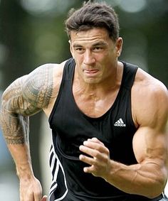 a man running with tattoos on his arm and chest, wearing a black tank top