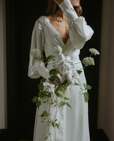 a woman wearing a white dress and holding flowers in front of her face while standing next to a window