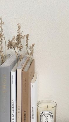 a candle and some books on a shelf next to a glass with flowers in it