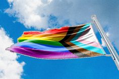 the rainbow flag is flying high in the blue sky with fluffy white clouds behind it