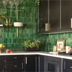 a kitchen with black cabinets and green tile backsplash, potted plants on the counter