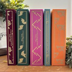 three books sitting on top of a wooden table next to a potted green plant