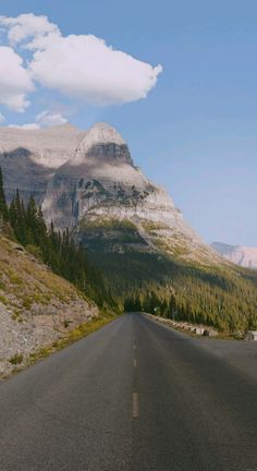 an empty road in the mountains with trees on both sides and a mountain behind it