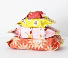 three pillows stacked on top of each other in different colors and patterns, one is pink, the other is yellow