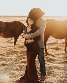 a pregnant woman standing next to a man in a cowboy hat and dress with horses behind her