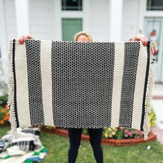 a woman holding up a black and white blanket in front of a house with her hands on the ground