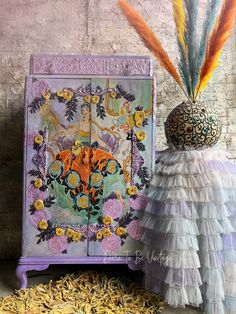 an artistically decorated cabinet next to a decorative vase with flowers and feathers on it