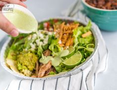 someone pouring dressing onto a salad in a bowl