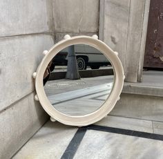 a round mirror sitting on the ground next to a building