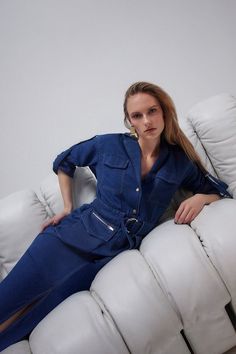 a woman in a blue jumpsuit sitting on a white couch with her legs crossed