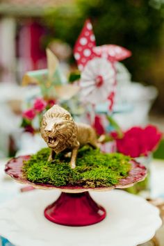 there is a small toy animal on top of a cake plate that has moss growing on it