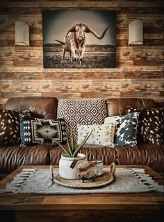 a living room with leather couches and cow artwork on the wall above it is a coffee table that has a potted plant in front of flowers