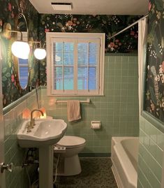 a bathroom with green tile and floral wallpaper