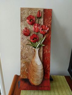 a vase filled with red flowers sitting on top of a table next to a wall