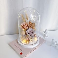 there is a glass dome with flowers in it on top of a book next to an angel figurine