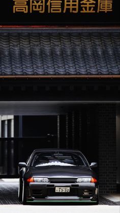 a black car parked in front of a building with chinese writing on the sign above it