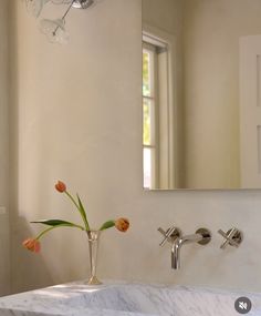 a vase with flowers in it sitting next to a mirror on the wall above a sink