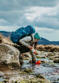 a woman with a blue backpack is wading in the water and holding a red object