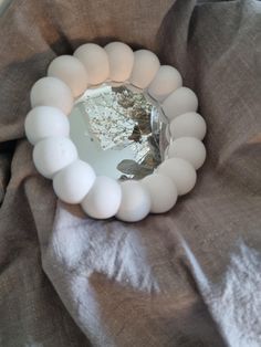 a white beaded bracelet sitting on top of a gray cloth next to a mirror