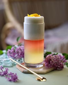 a tall glass filled with liquid sitting on top of a table next to purple flowers