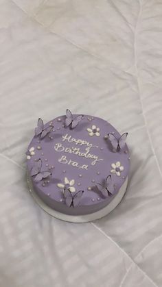 a birthday cake with purple frosting and white flowers on the top is sitting on a bed