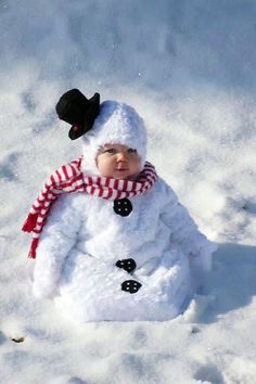 a baby wearing a snowman hat and scarf sitting in the snow