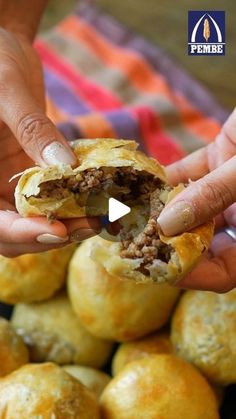 two hands holding a meat filled pastry in front of a pile of other pastries