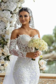 a woman in a white wedding dress holding a bouquet of flowers and posing for the camera