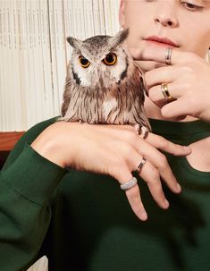 a woman is holding an owl in her hands while wearing two wedding rings on her finger