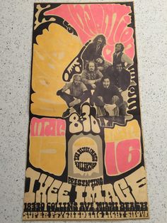 an old concert poster hanging on the wall in front of a white wall with pink and yellow designs