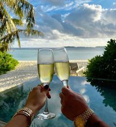 two people toasting with wine glasses in front of an outdoor swimming pool and palm trees